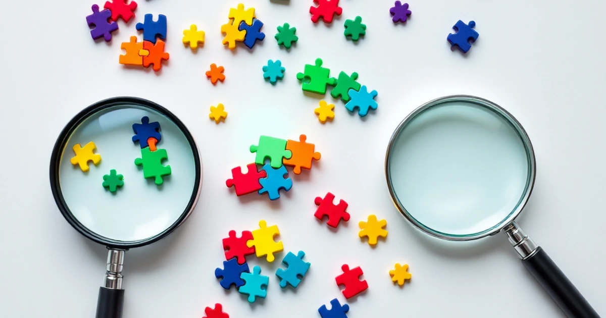 A flat lay of colorful puzzle pieces with one glowing green piece and a magnifying glass.
